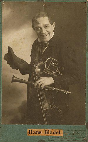 Hans Blädel, mit Trompete, Klarinette, Violine und Hut in der Hand, um 1910